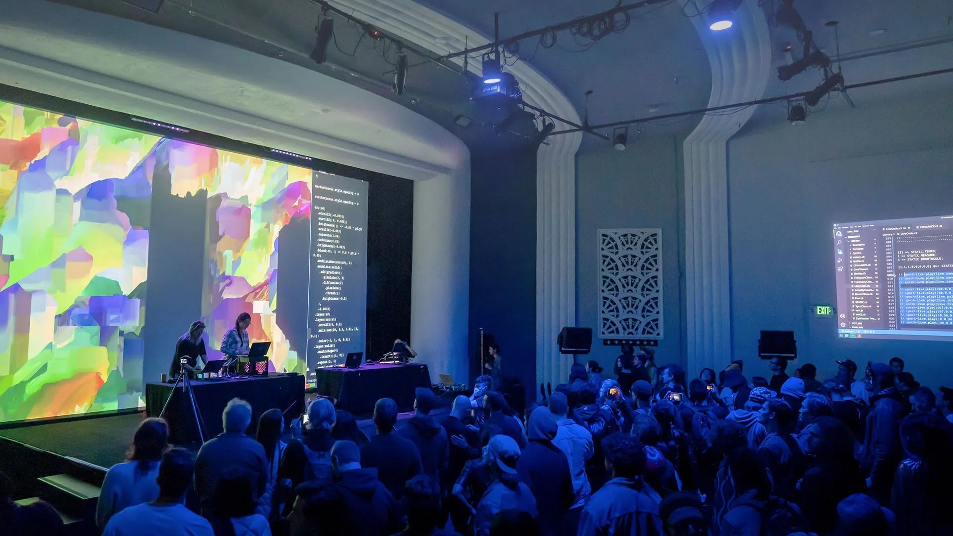 image of people sitting at a concert facing a colorful screen