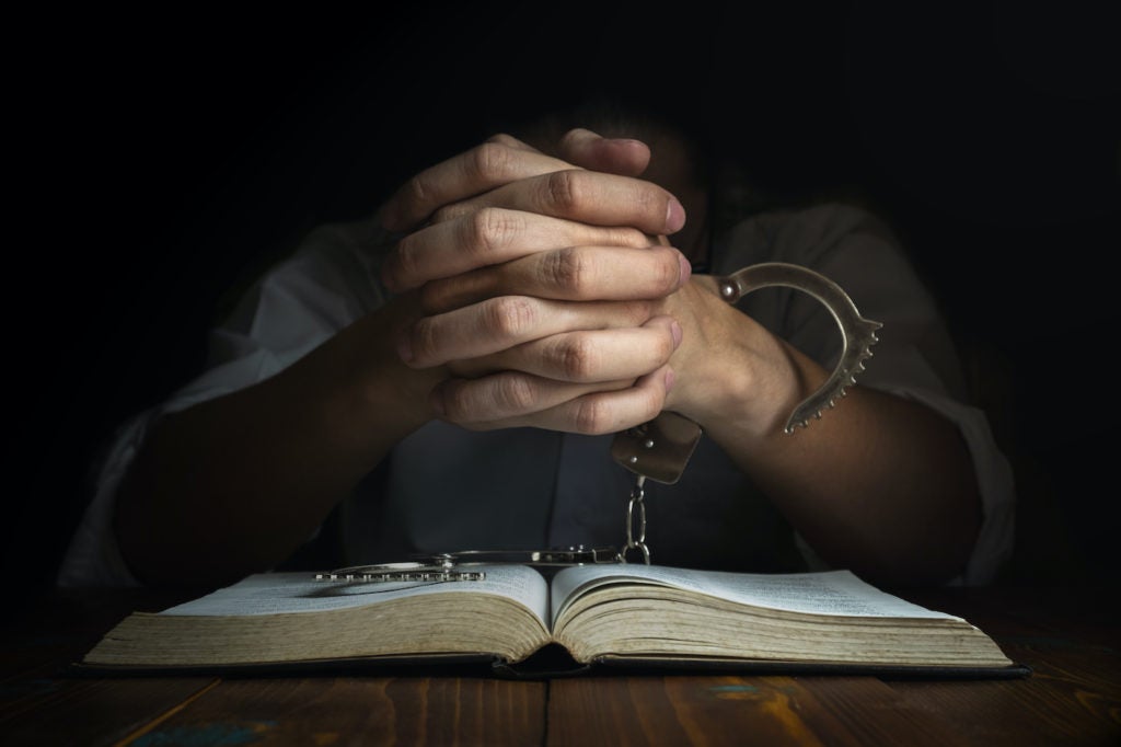 image of a prison inmate's hands clasped together over a book